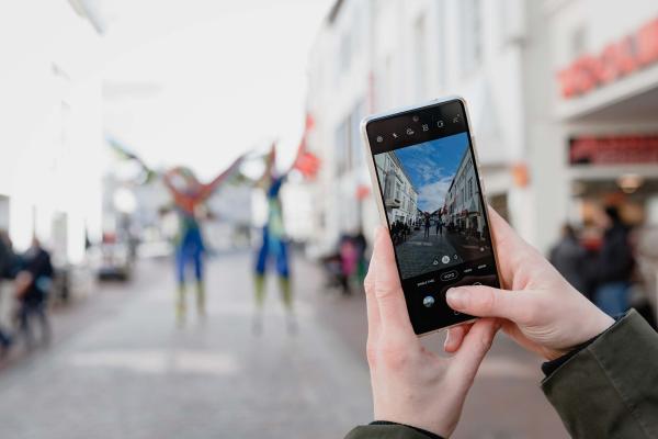 Eine Person macht mit seinem Handy ein Foto von Stelzenkünstlern in der Innenstadt